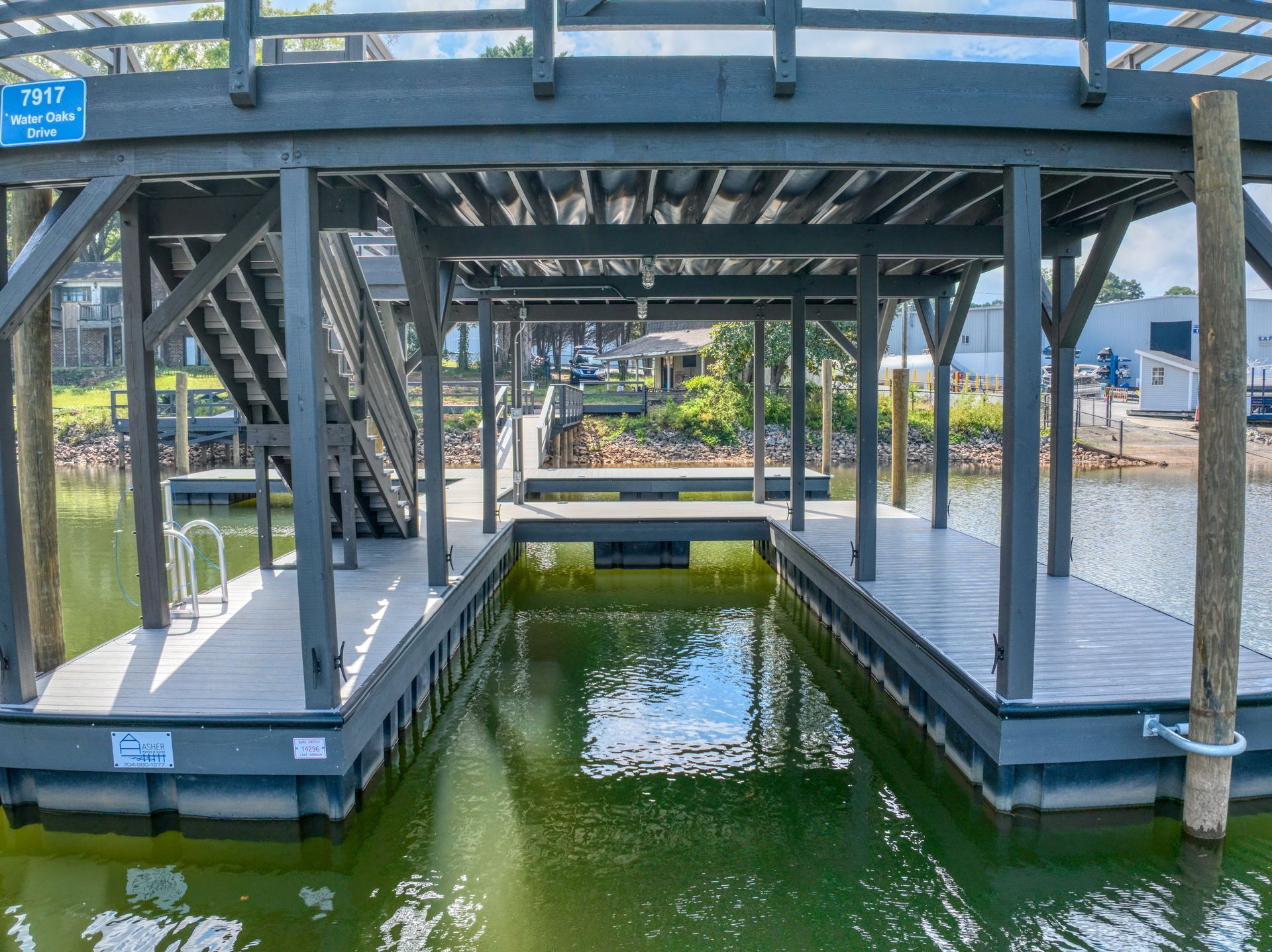 Dock with dark gray roof, stairs, and watercraft slips. Located on a lake, with trees visible in the background.