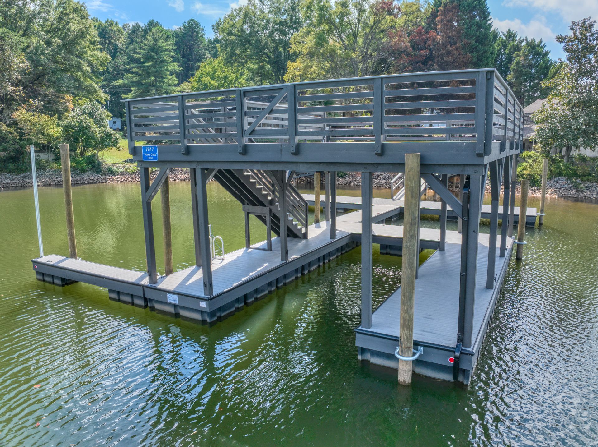 Dock with a multi-level platform, steps, and handrails extending over a lake. Gray and white colors.