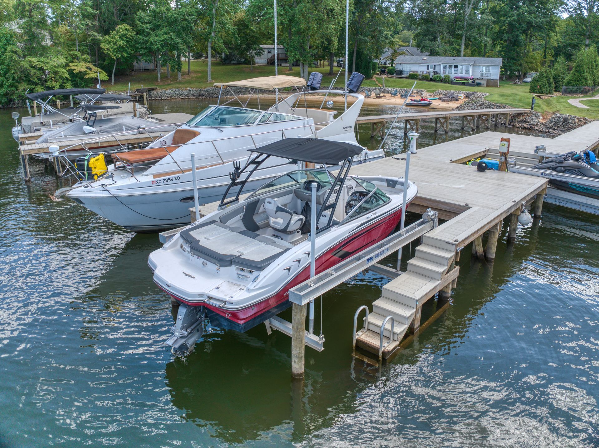 Boats docked at a pier on a lake. Red and white motorboat on a lift, other boats alongside.