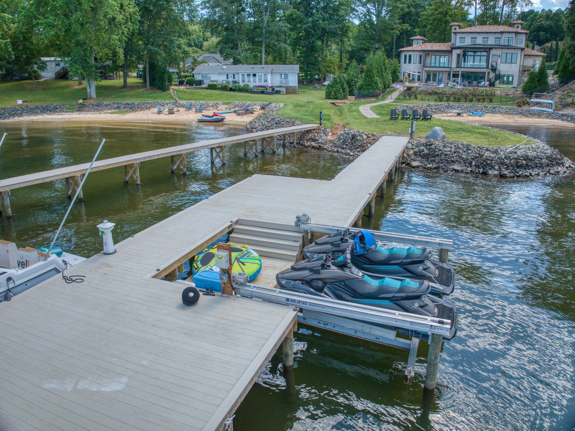 Dock with jet skis and kayaks, overlooking a lake with houses in the background.