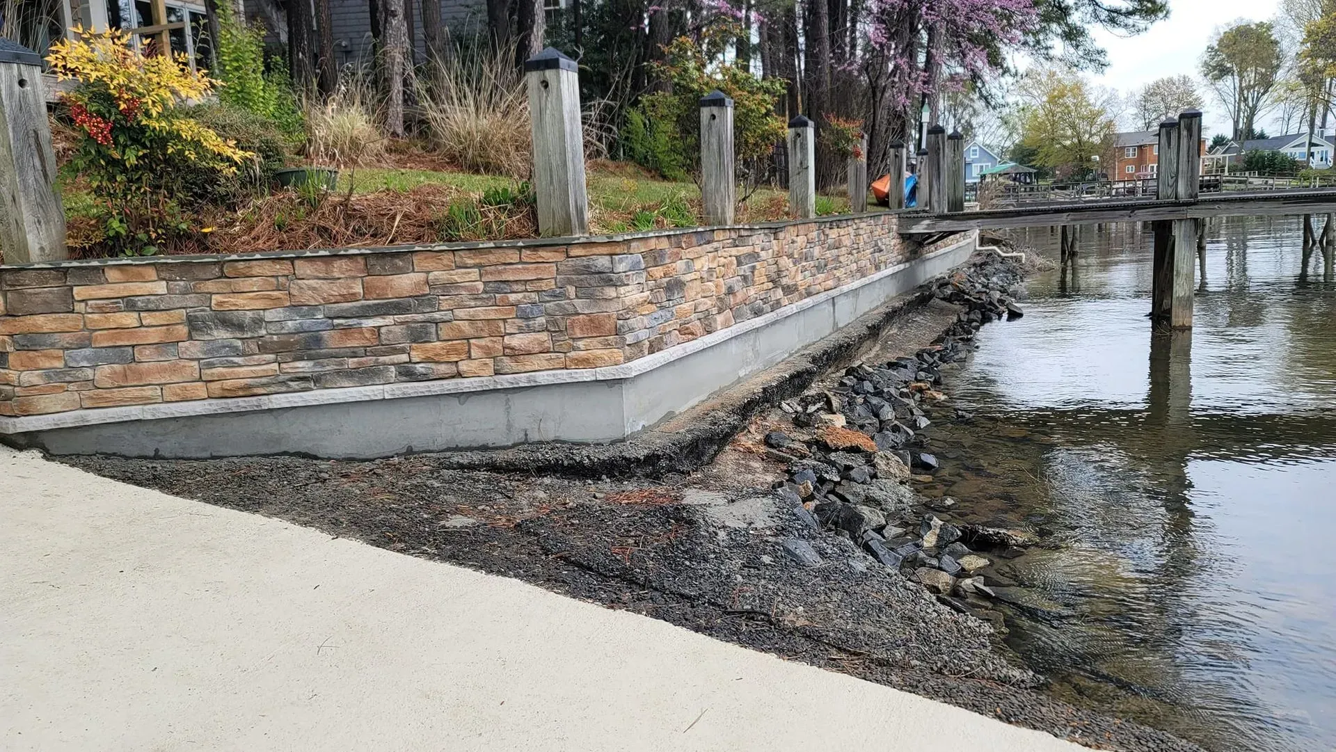 Stone and concrete seawall at water's edge, with wood posts behind.