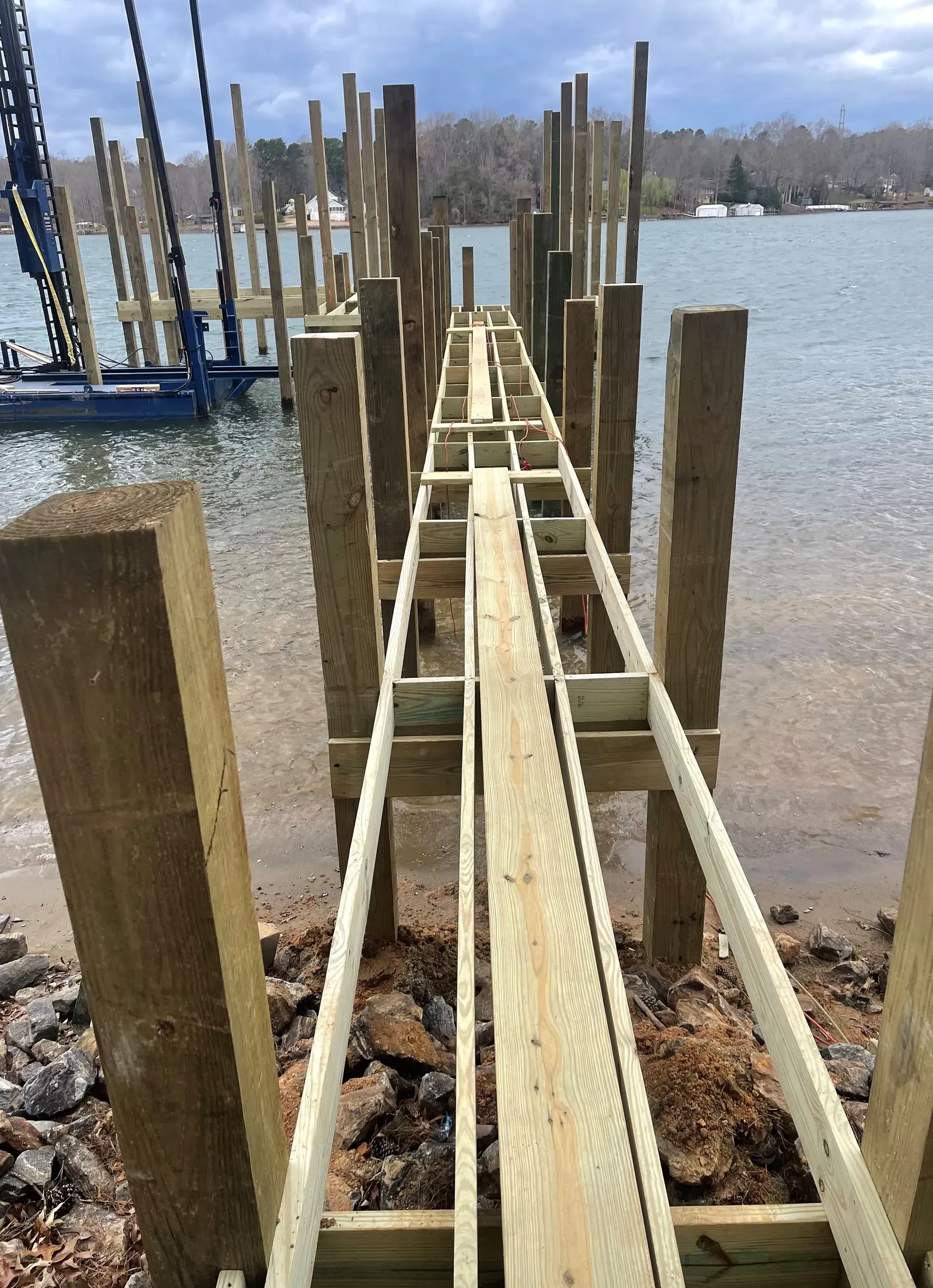 Construction of a wooden pier over water with wooden posts and framing.