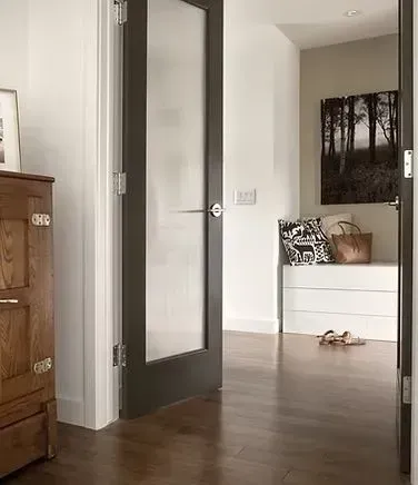 A doorway with frosted glass, revealing a hallway with a bench, artwork, and wood flooring.