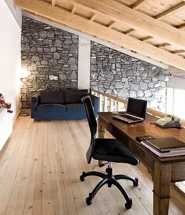 Home office with stone accent walls, wooden desk and beams, blue sofa.