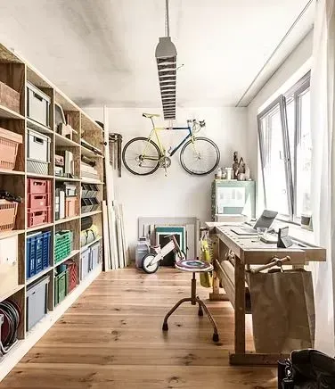 Home office with wooden shelving, bike, desk, and window. Natural light fills the space.