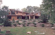 A large wooden house is sitting on top of a hill in the middle of a forest.