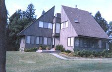 A large house with a triangle shaped roof is surrounded by trees.