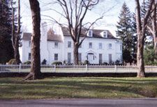 A large white house with a white picket fence and trees in front of it.