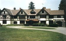 A large house with a lot of windows is sitting on top of a lush green field.