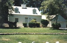 A white house with a white roof is sitting on top of a lush green lawn.