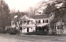 A black and white photo of a large house surrounded by trees.