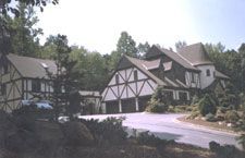A large house with a car parked in front of it is surrounded by trees.