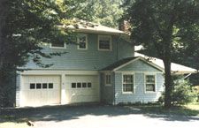 A house with a garage and a porch is surrounded by trees.