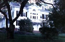 A large white house is surrounded by trees and bushes.