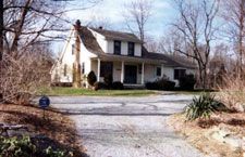 A white house with a porch and a driveway in front of it.