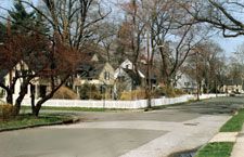 A residential neighborhood with a white picket fence and trees on the side of the road.