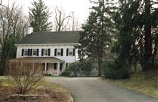 A large white house with a driveway leading to it is surrounded by trees.