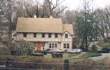 A white house with a brown roof is surrounded by trees and a fence.