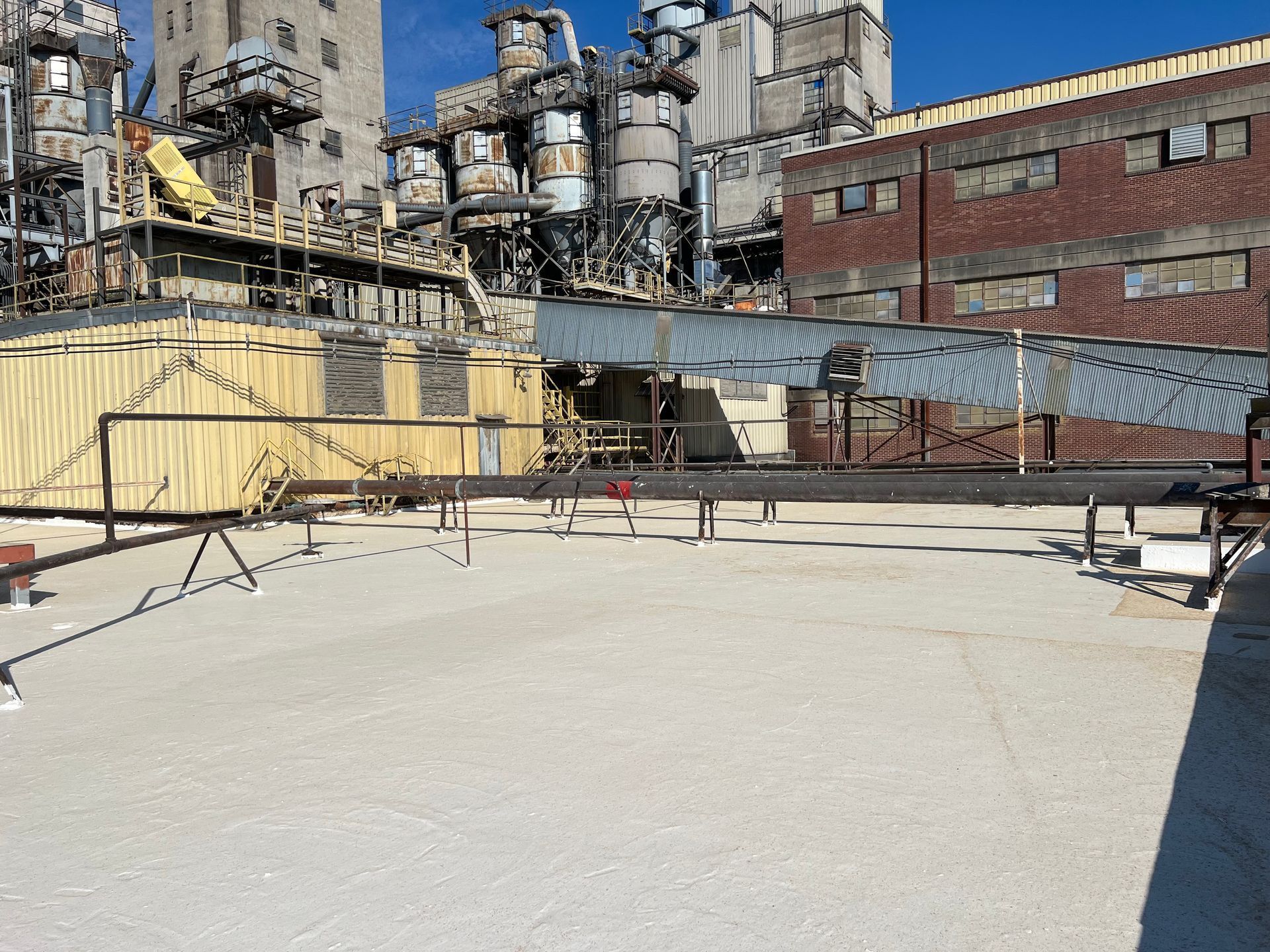 Industrial rooftop with complex of metal structures and buildings against a clear blue sky.