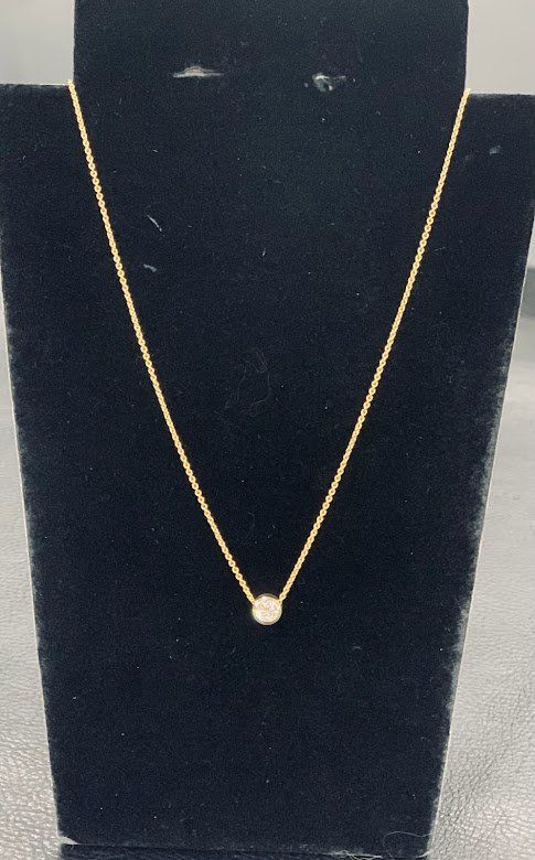 A gold necklace with a single diamond on a black mannequin