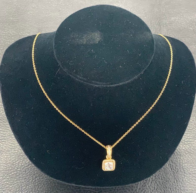A gold necklace with a square pendant on a black mannequin