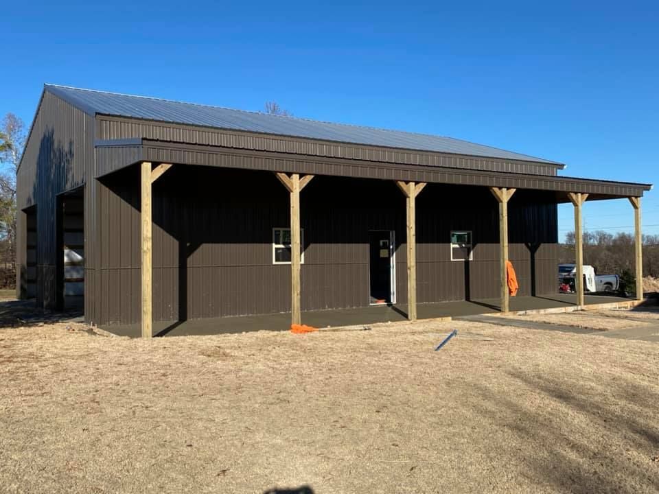 Brown metal barn with a porch, wooden supports, and a clear blue sky.