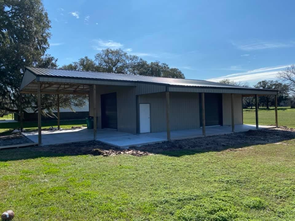 A light-colored metal building with a covered porch, on a grassy field under a blue sky.