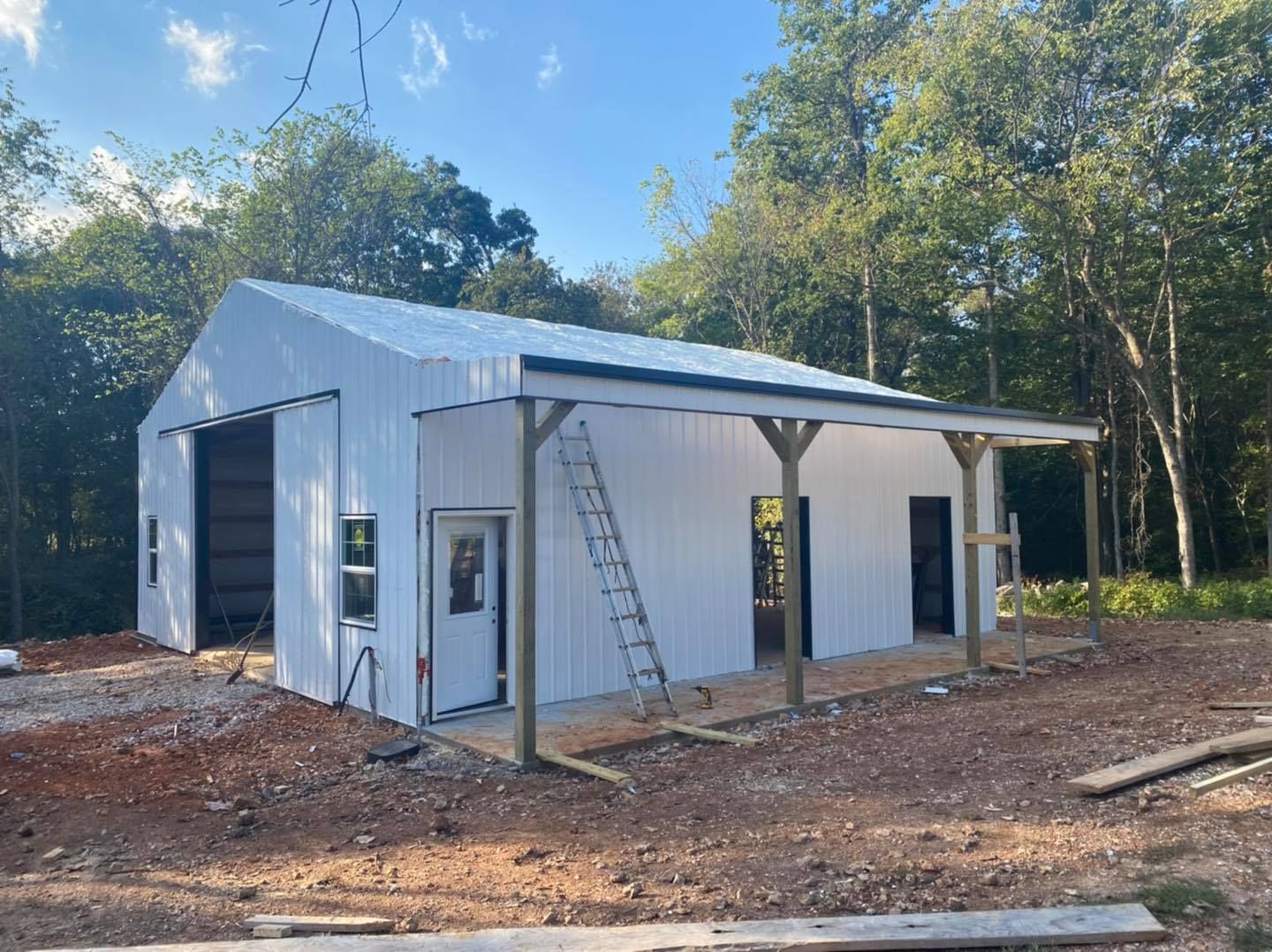 White building with a porch under construction in a wooded area.