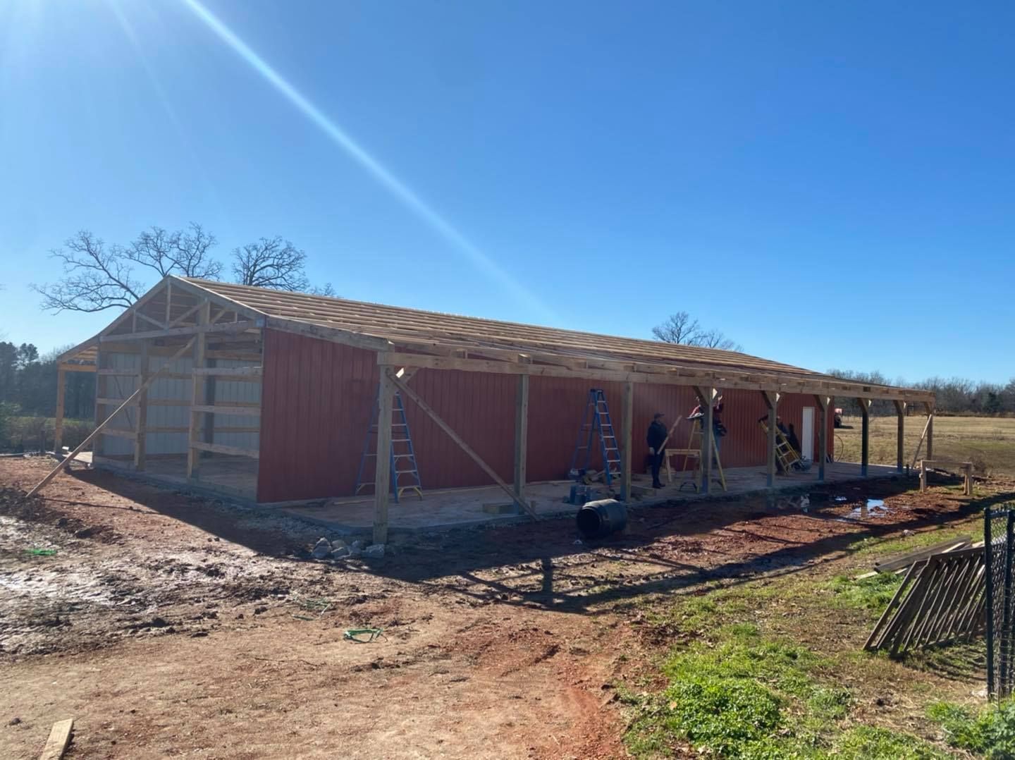A red barn under construction on a sunny day, with workers and scaffolding visible.