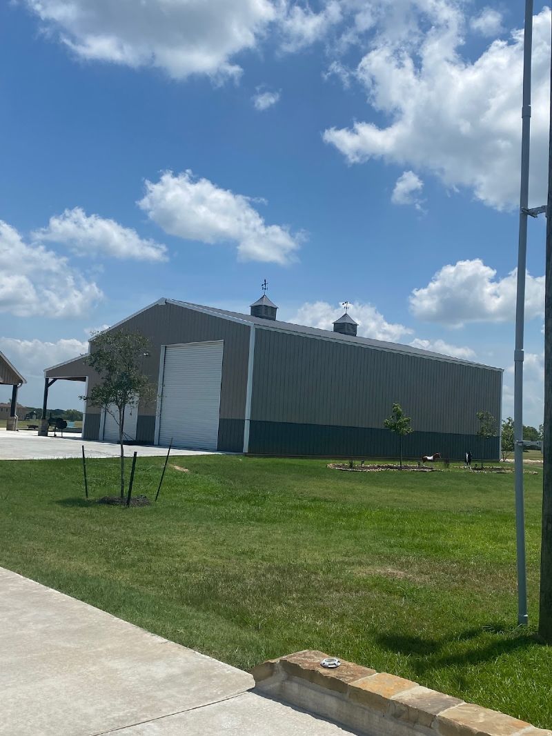 Large gray metal building with white door under a blue sky and green grass.