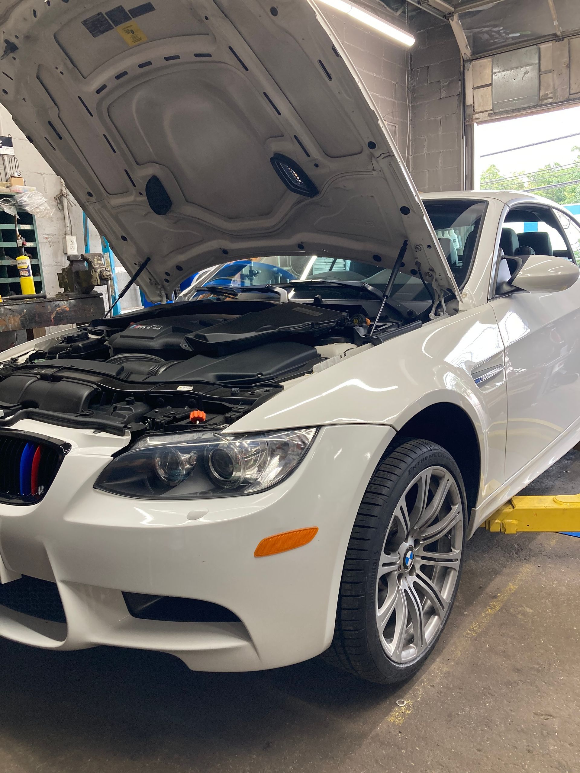 White BMW sedan in an auto shop with its hood open for inspection or repair.