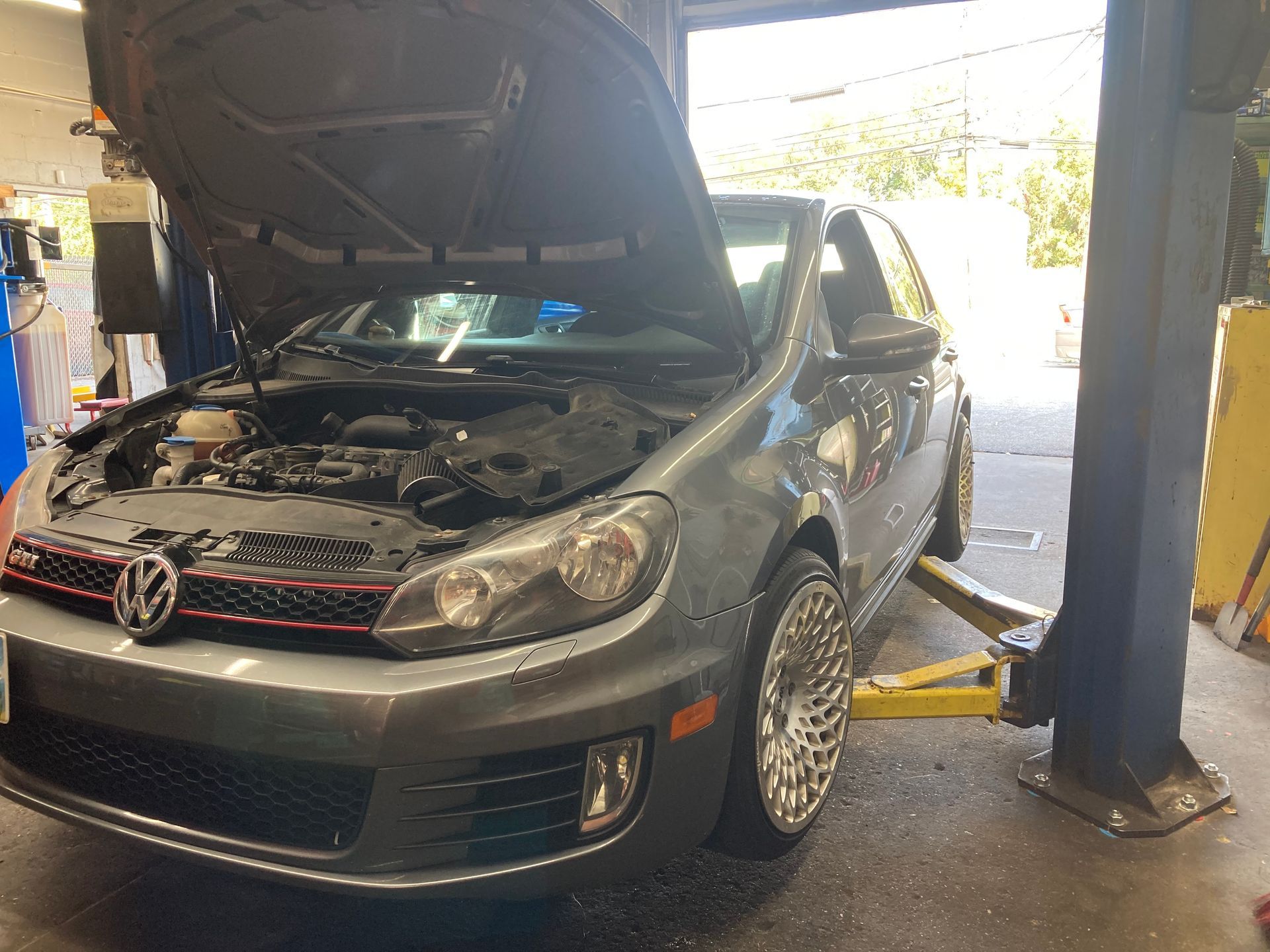 Gray Volkswagen with hood open on a lift in an auto repair shop