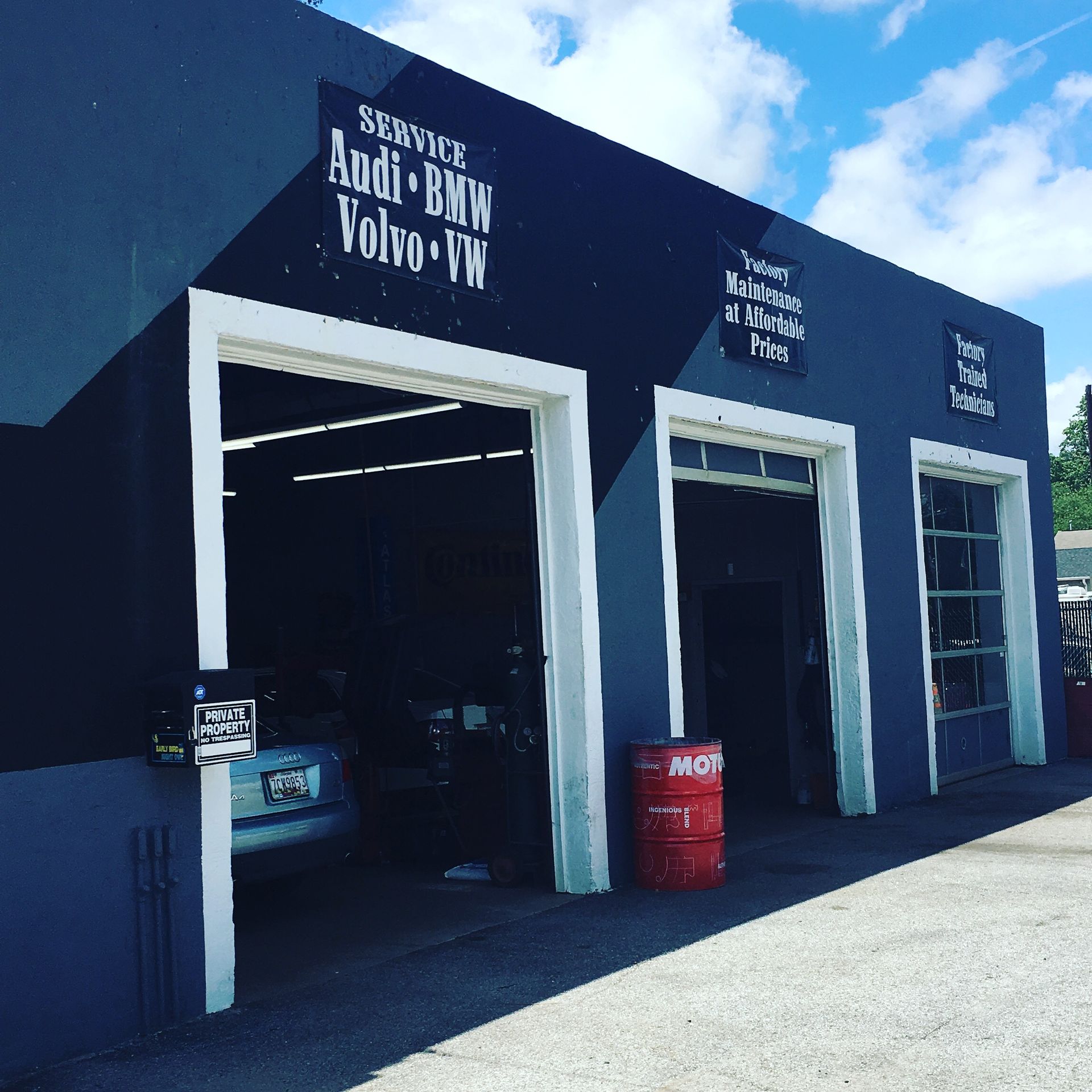 Blue auto shop with three open bays, white trim, and signs for service, batteries, and tires.