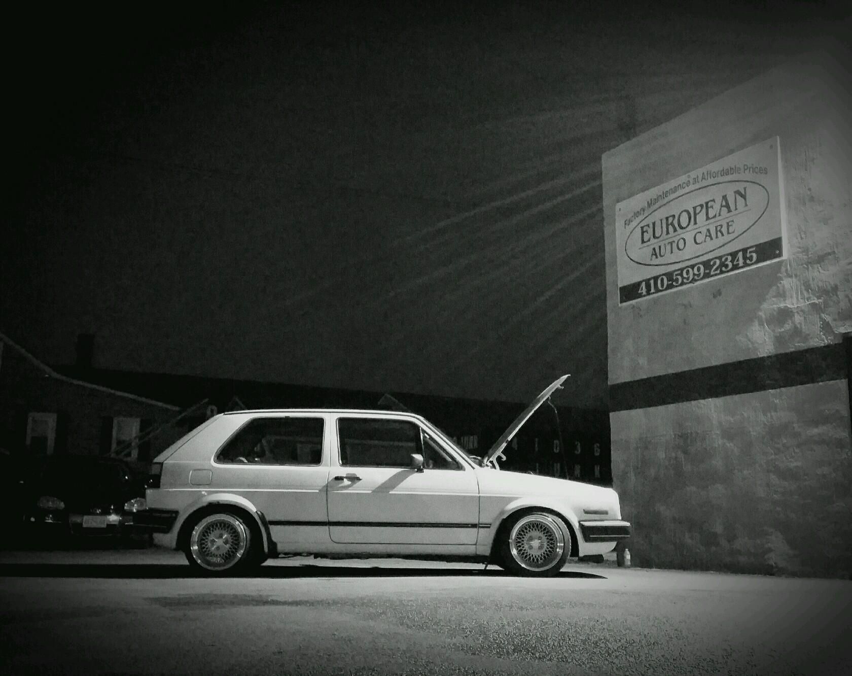 White hatchback parked beside a building at night with its hood open.