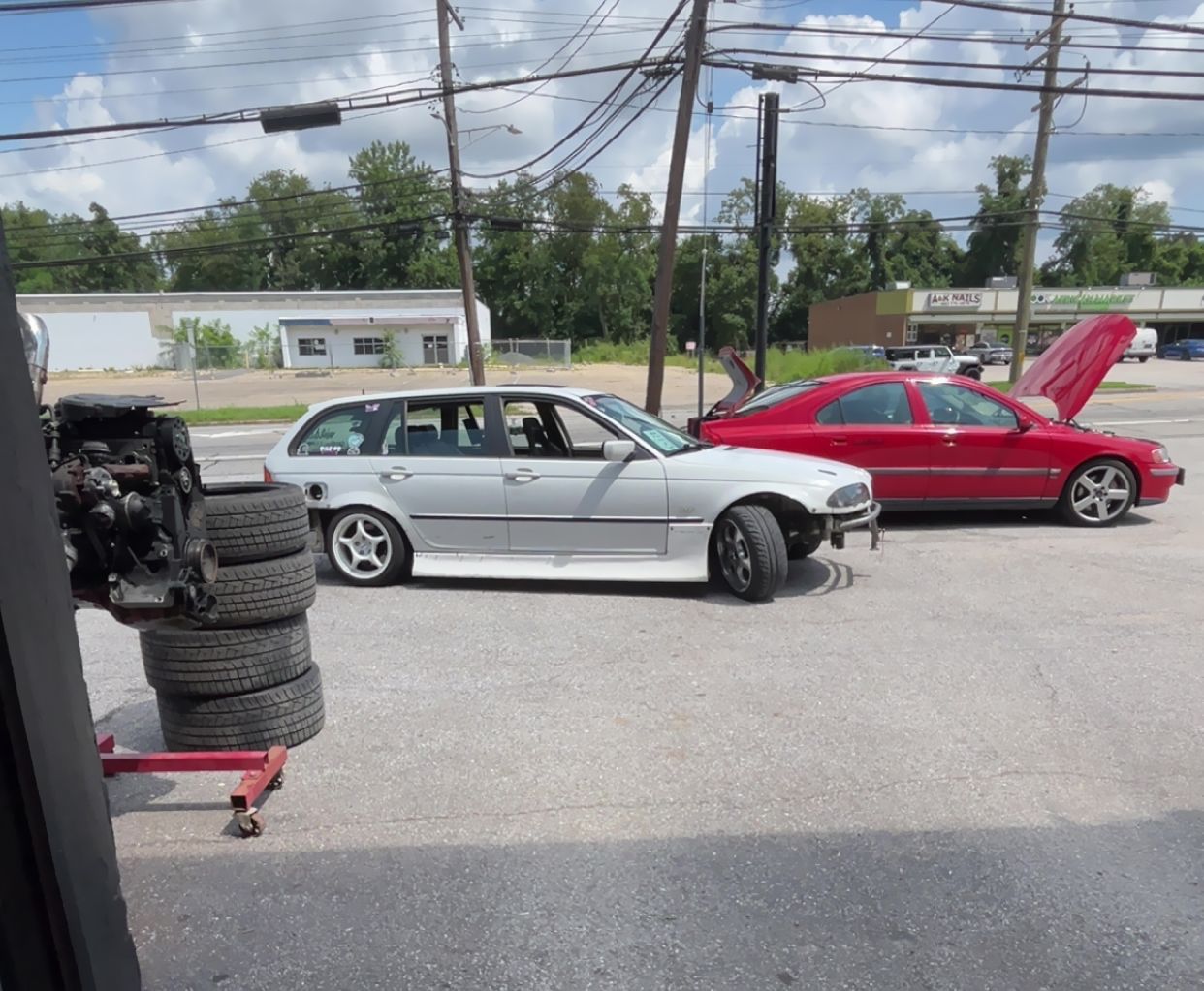 Two parked cars, silver and red, in a lot with a stack of tires in the foreground