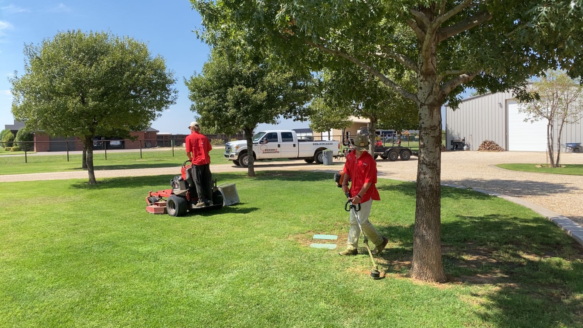 Two people in red shirts mowing grass with a riding mower and weed eater on a sunny day.