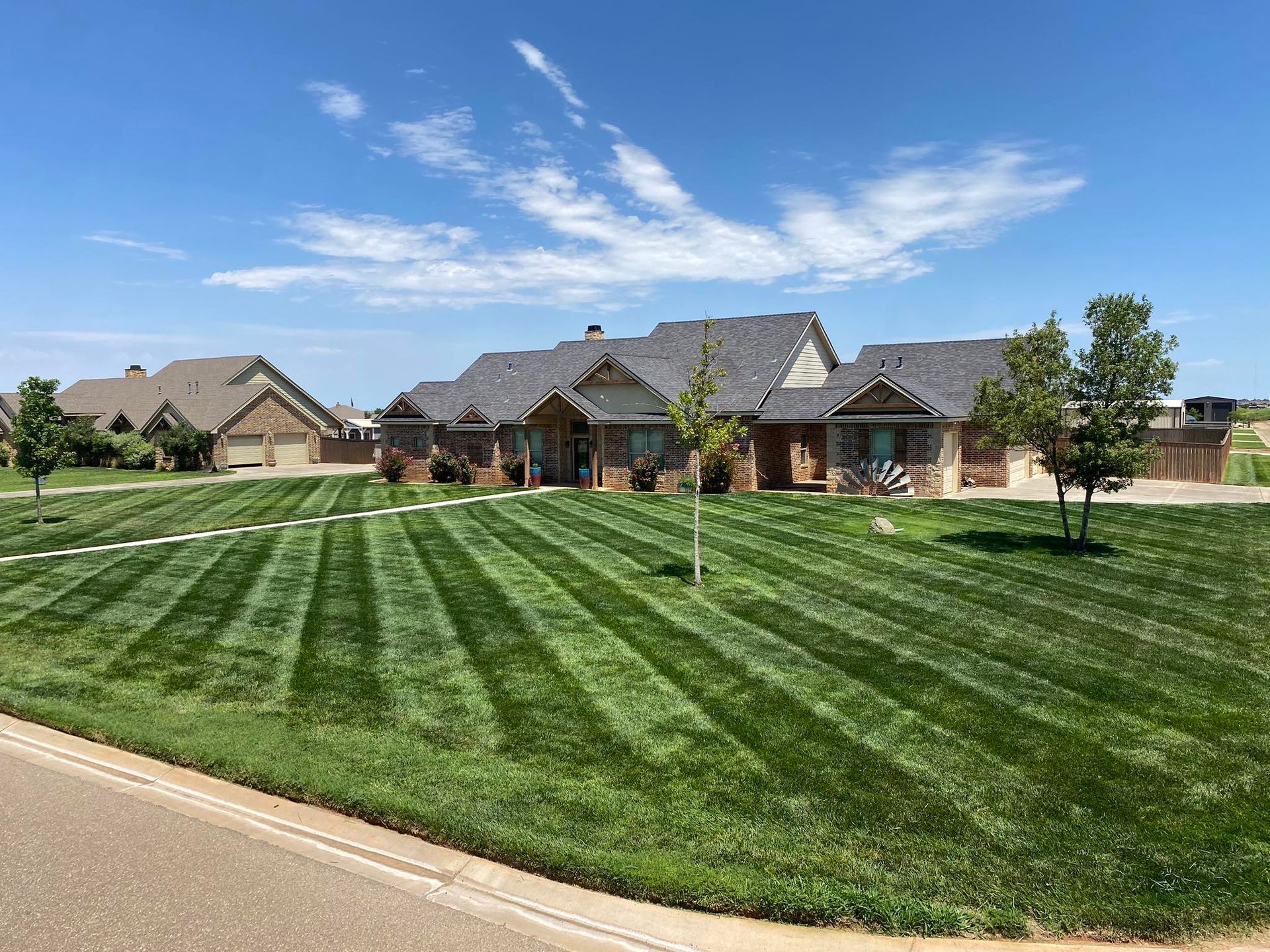 A large brick house with a neatly striped lawn under a bright blue sky with clouds.