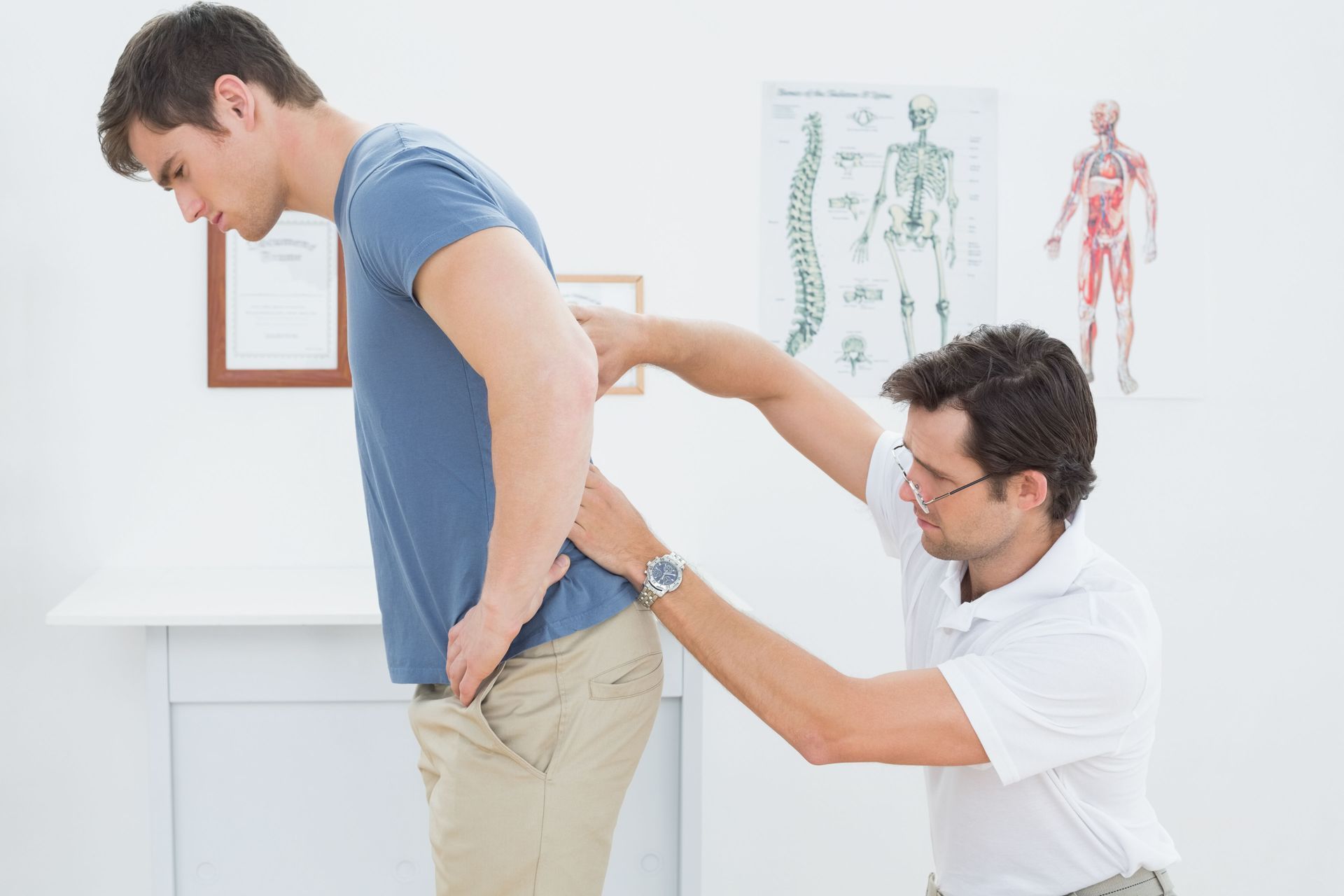 Man being examined by chiropractor for back pain. Light-skinned individuals, indoor setting.