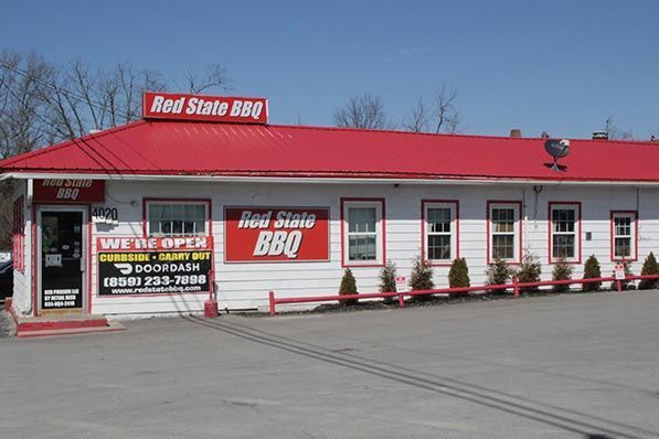 A Red State BBQ restaurant building with white siding, a red roof, and a large sign in a paved parking lot.