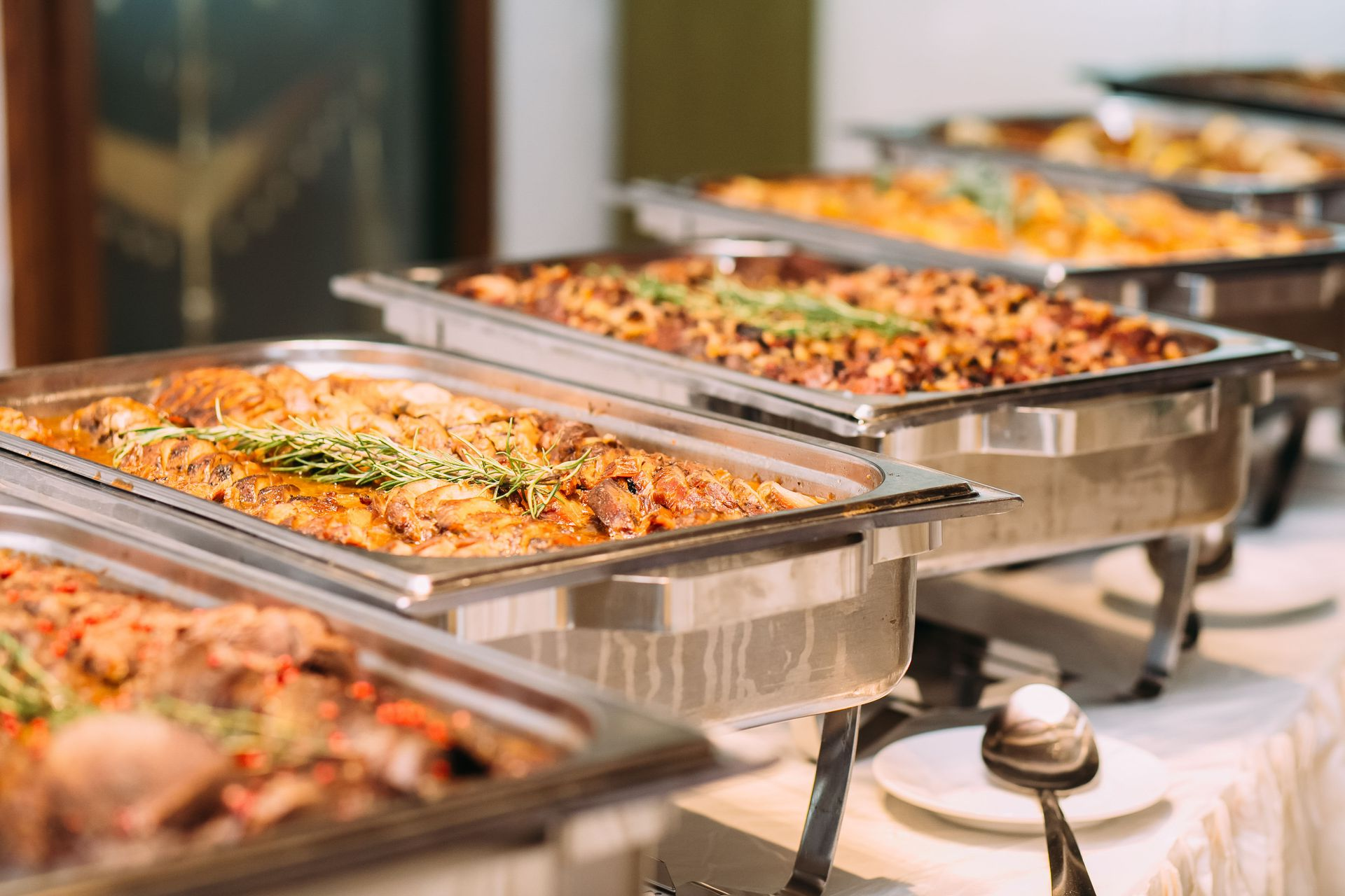 A buffet table featuring a row of stainless steel chafing dishes filled with various prepared food items.
