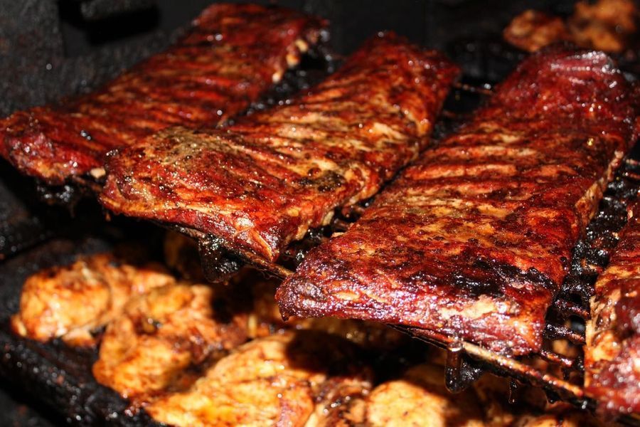 Racks of seasoned, glazed ribs grilling on a barbecue rack above pieces of chicken.