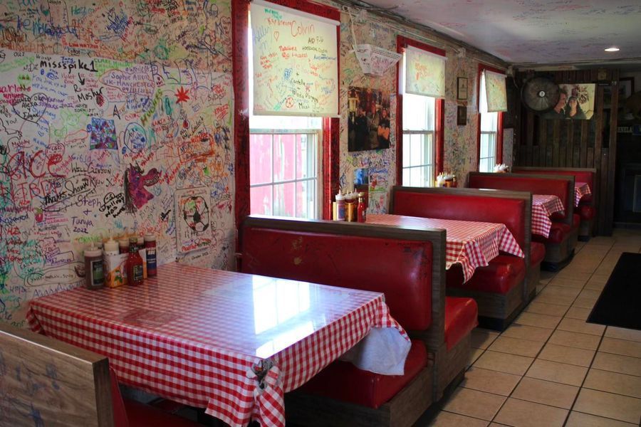A restaurant interior with red vinyl booths, checkered tablecloths, and walls covered in customer graffiti.