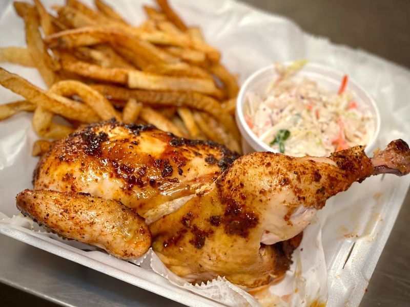 A half-roasted chicken with seasoned skin, served with a side of french fries and coleslaw in a white takeout container.