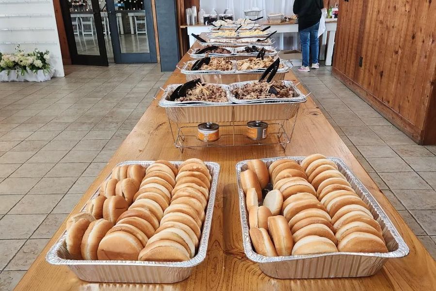 A buffet table featuring two large trays of halved bread rolls in the foreground and chafing dishes with food behind them.