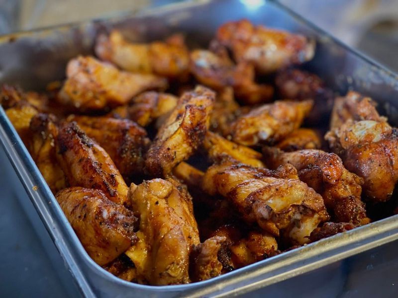 A metal container filled with cooked, golden-brown chicken wings seasoned with spices.