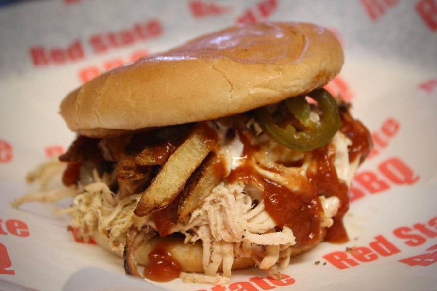 A pulled pork sandwich with fries, jalapeños, and barbecue sauce on branded 