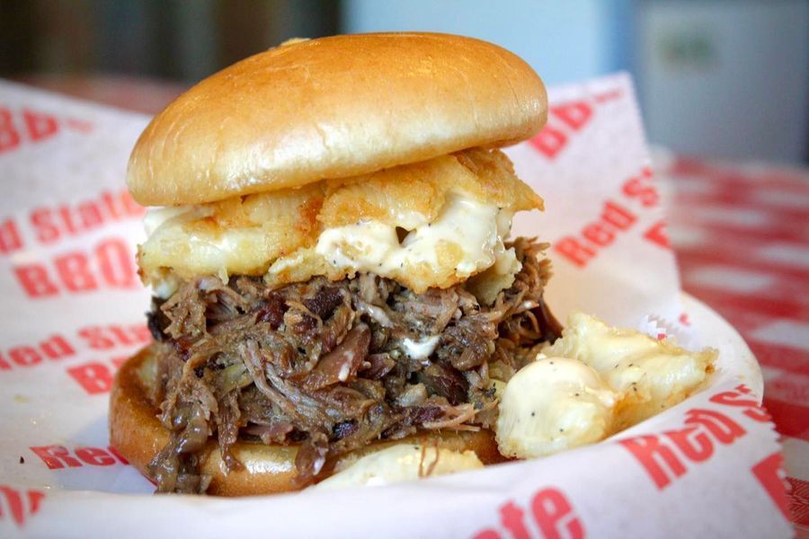 A pulled pork sandwich topped with fried cheese curds on Red State BBQ branded paper.