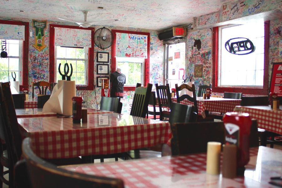 A restaurant interior with red-and-white checkered tablecloths and walls covered in handwritten signatures and graffiti.