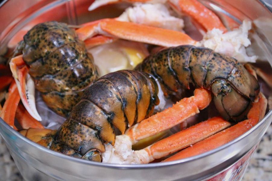 Raw lobster tails and crab legs nestled together inside a round metal container.