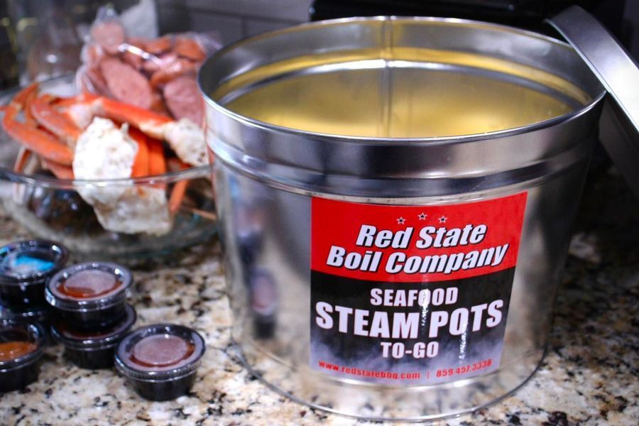 A Red State Boil Company seafood steam pot metal container sits on a counter next to a bowl of crab legs and dipping cups.
